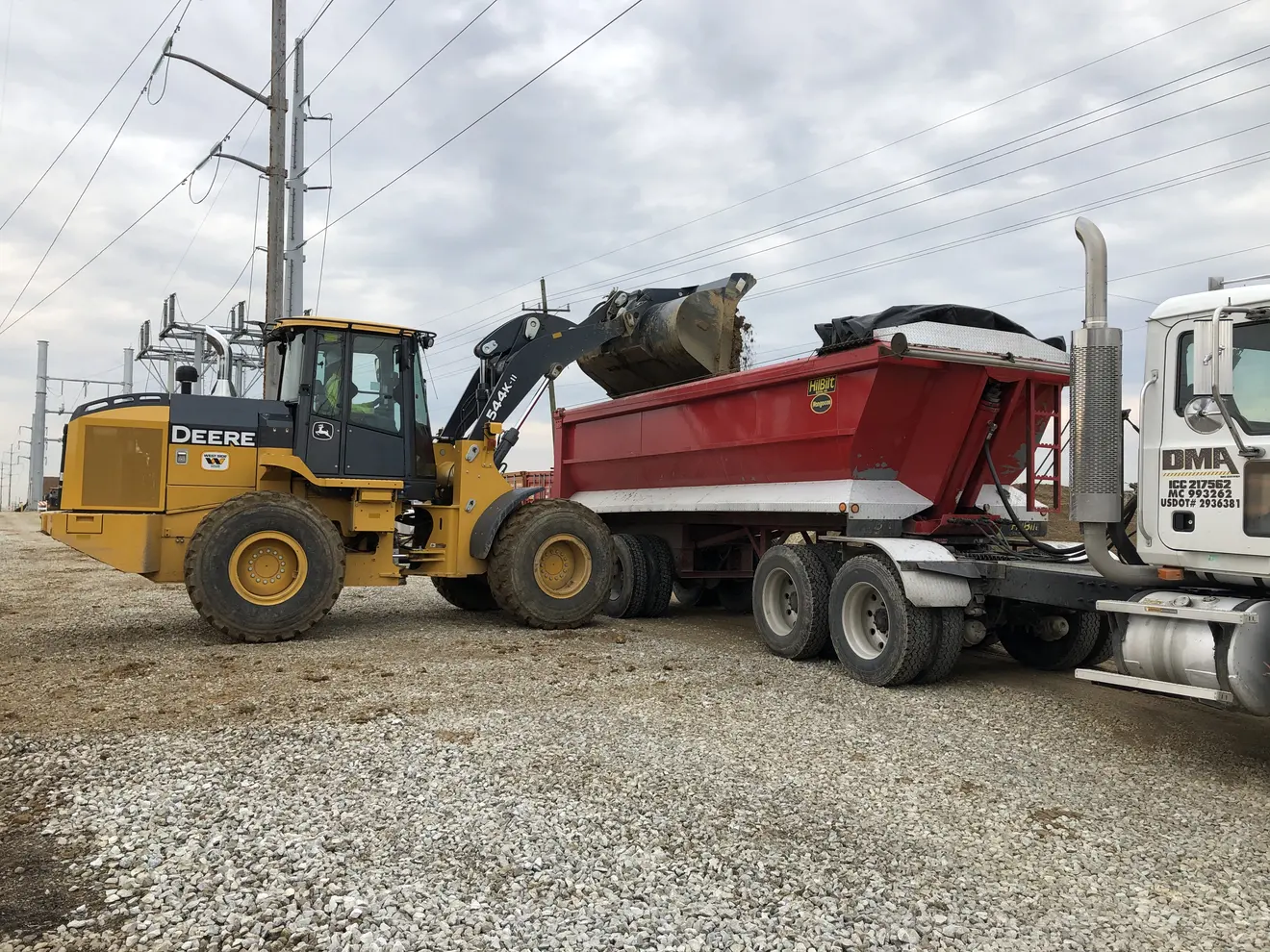 A loader transferring excavated soil into a roll-off container — material bound for a CCDD or clean-fill facility once classified