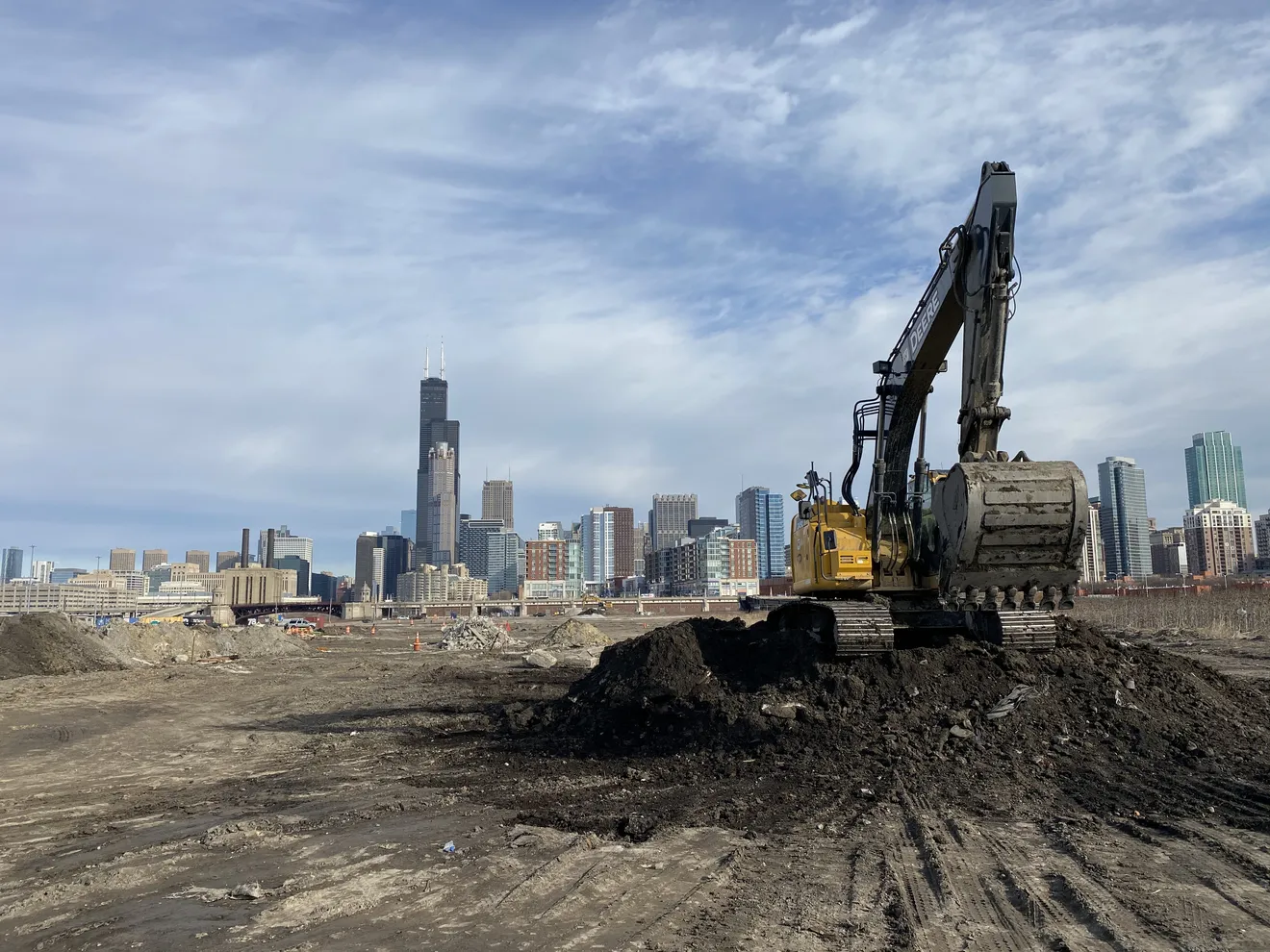 An excavator working a soil stockpile on a Chicago redevelopment site — material staged for classification and clean-fill haul-off