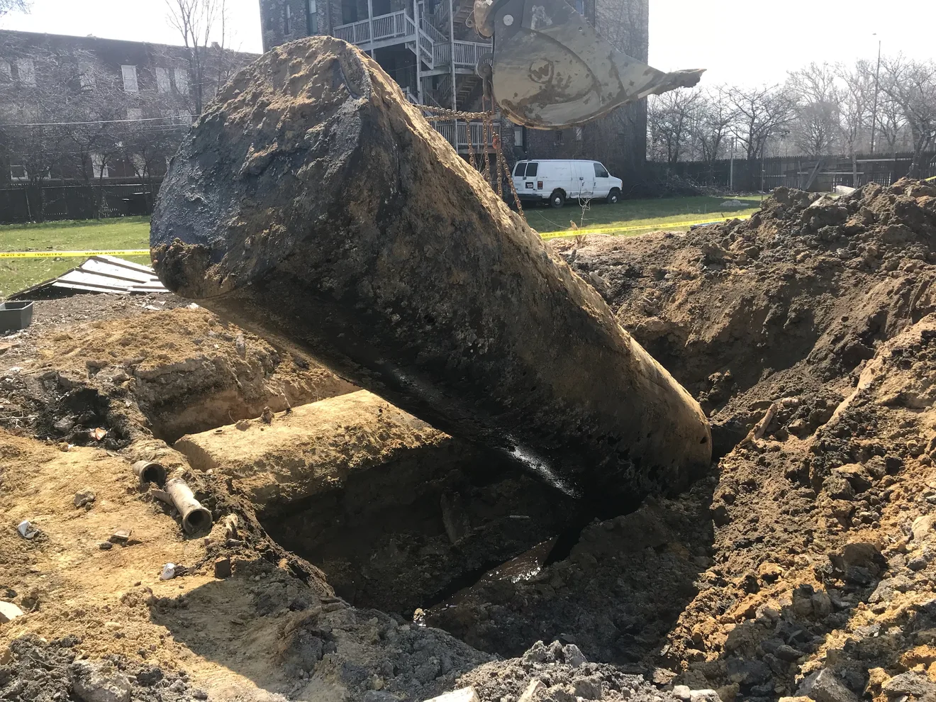 A corroded steel underground storage tank coated in petroleum residue being hoisted from the ground — evidence of a tank release