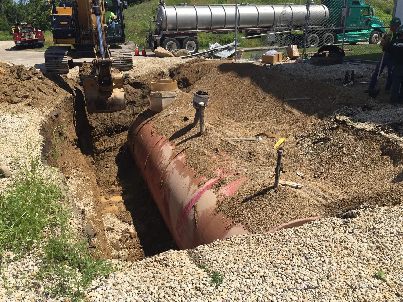 An exposed underground storage tank in an open excavation beside a vacuum tanker truck during removal