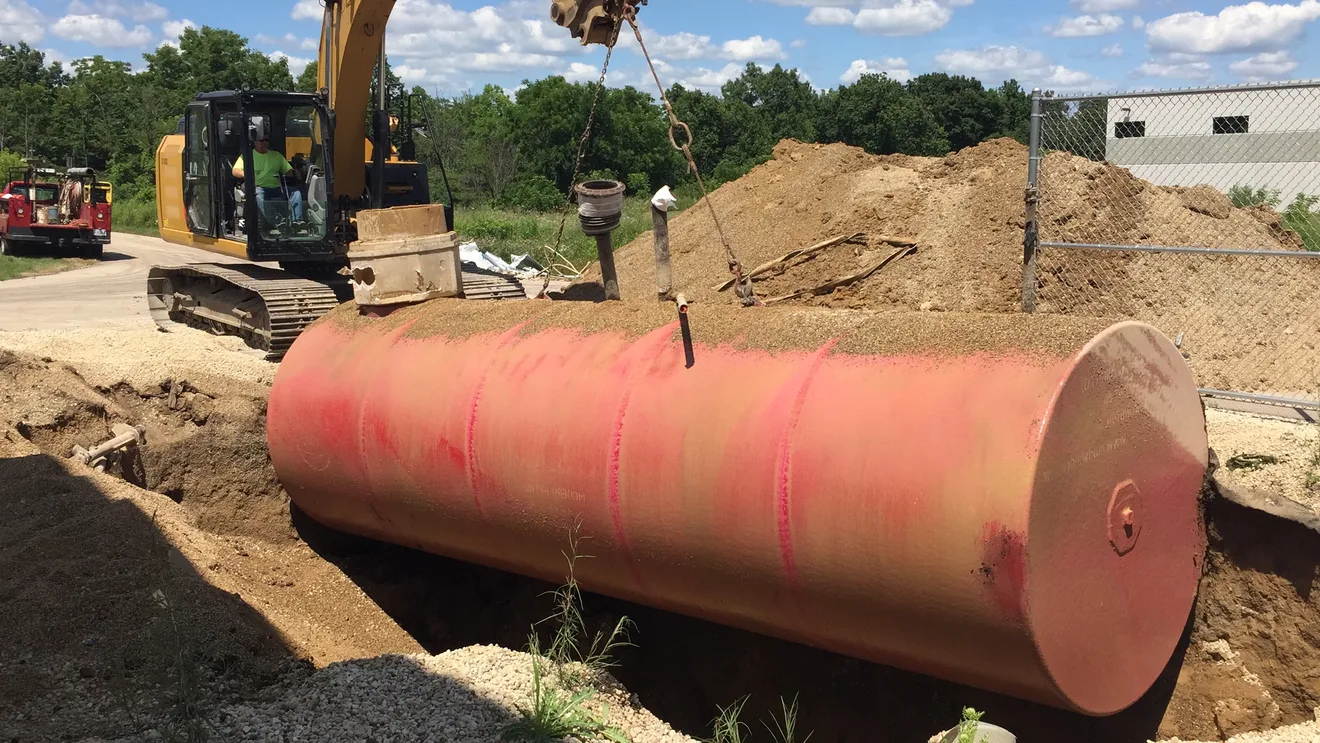 An excavator lifting a decommissioned underground storage tank out of the ground during a tank removal